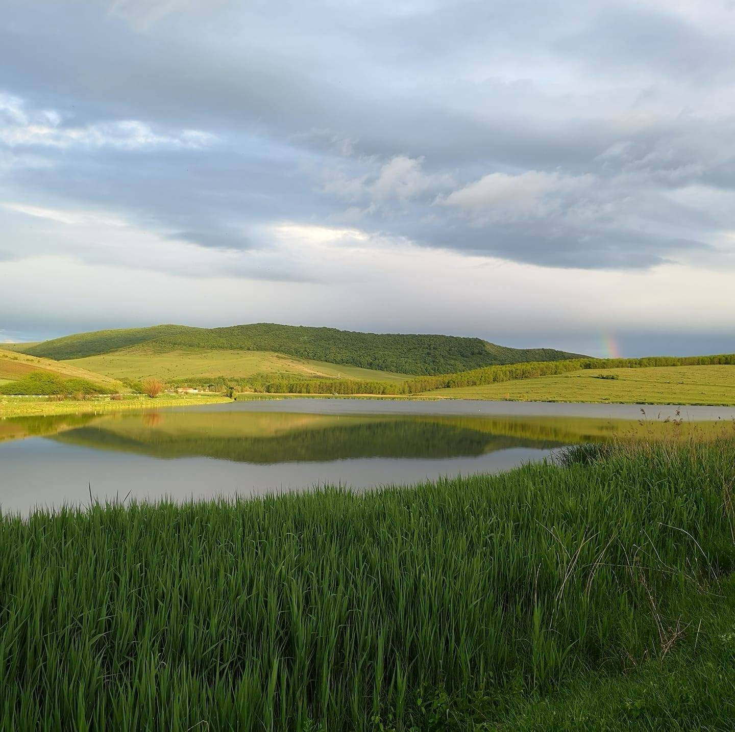 Lacul Sucutard-Chiriș la apus, cu dealuri verzi și un curcubeu